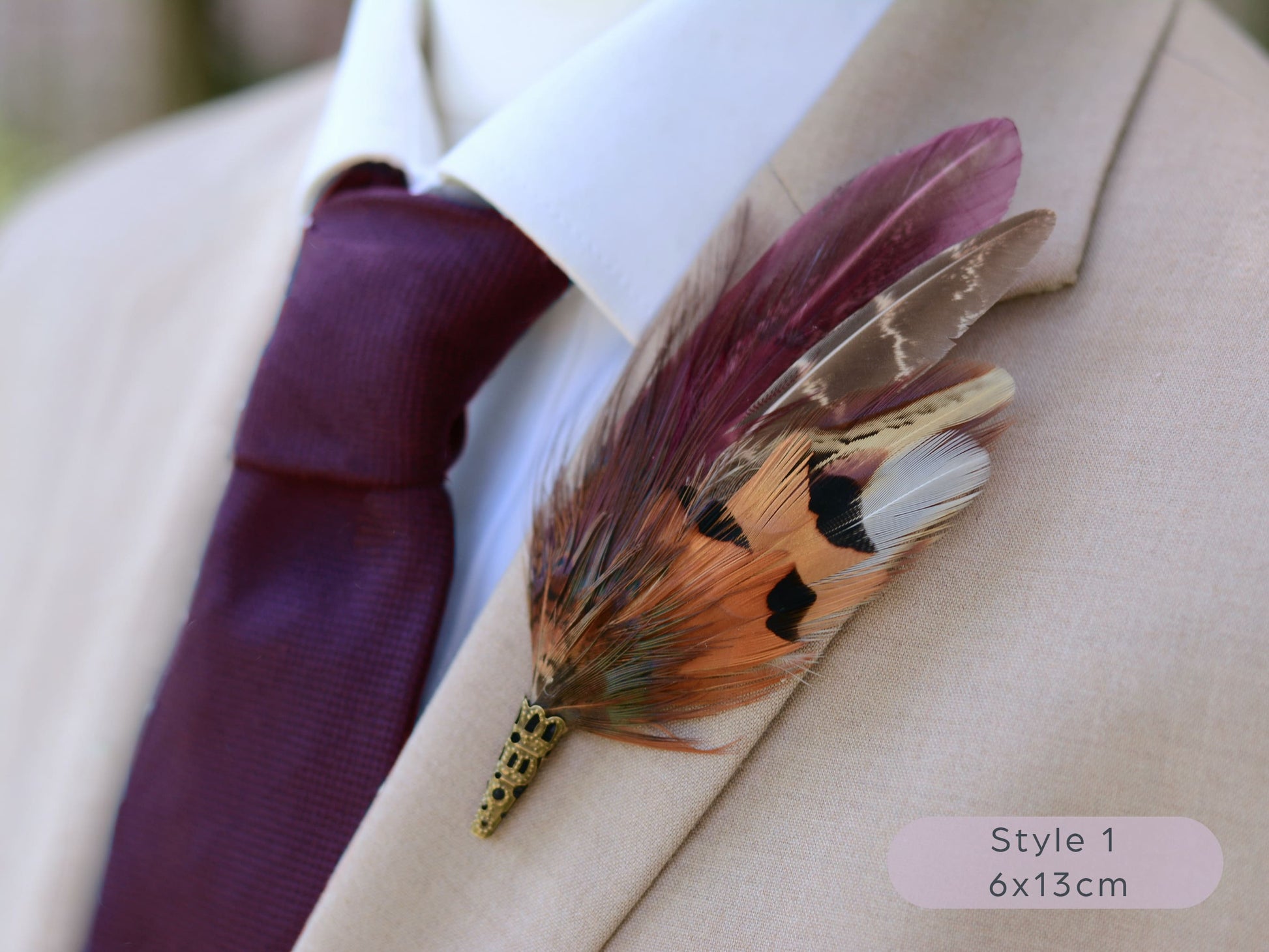 Maroon and pheasant feather lapel pin accessory on a beige suit jacket with a maroon tie from a side view