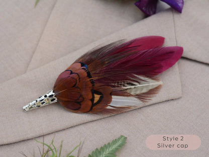 Burgundy and purple feathere brooch with a silver cap on a beige fabric background
