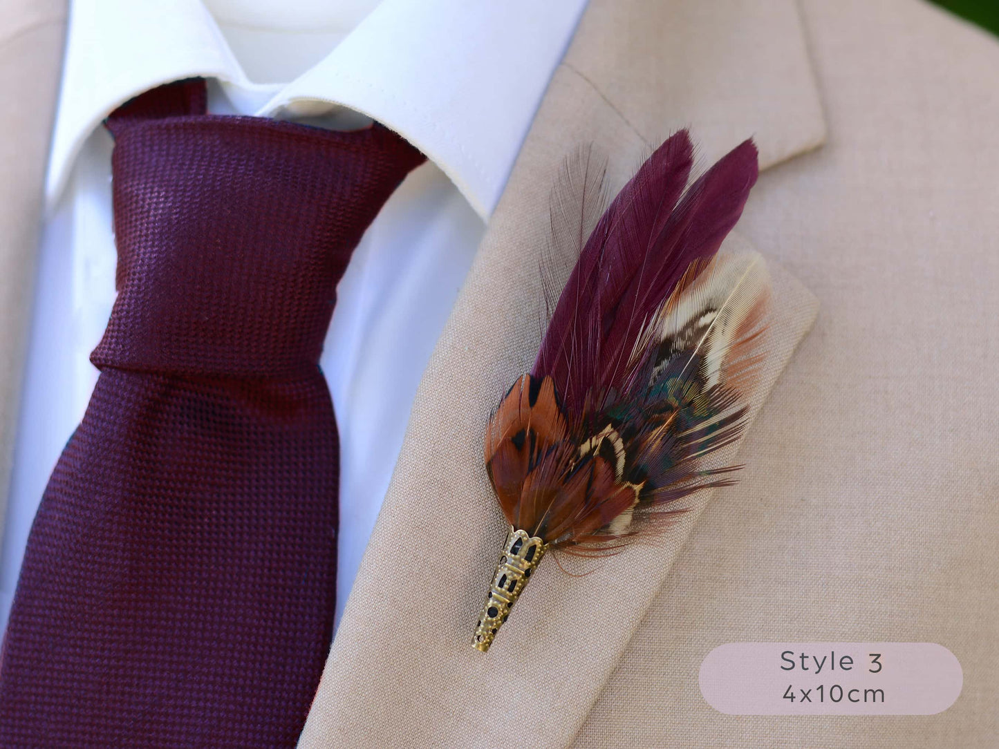 Maroon and pheasant feather lapel pin on a beige suit jacket with a maroon tie.