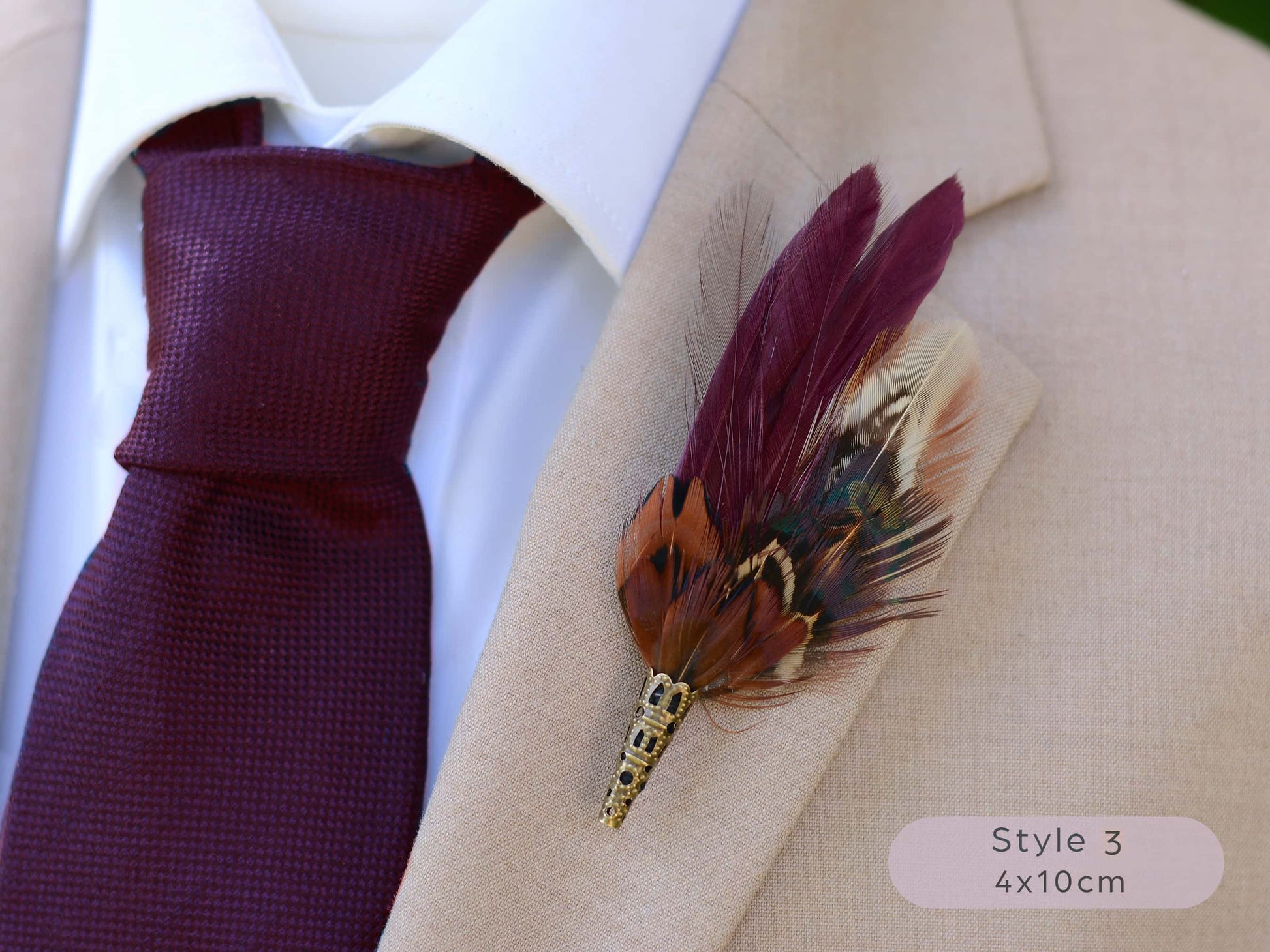 Maroon and pheasant feather lapel pin on a beige suit jacket with a maroon tie.