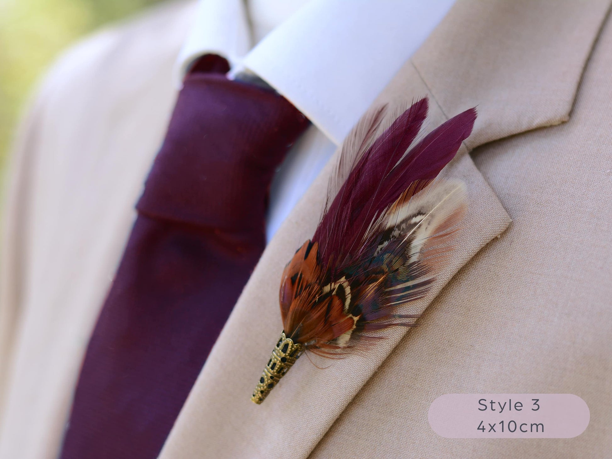 Maroon and pheasant feather lapel pin on a beige suit jacket with a maroon tie.