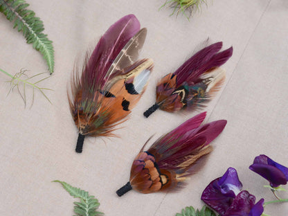 Three feathered wedding boutonnieres on a beige fabric background surounde by flowers and plants