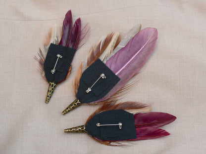 Three feathered brooches on a beige fabric background