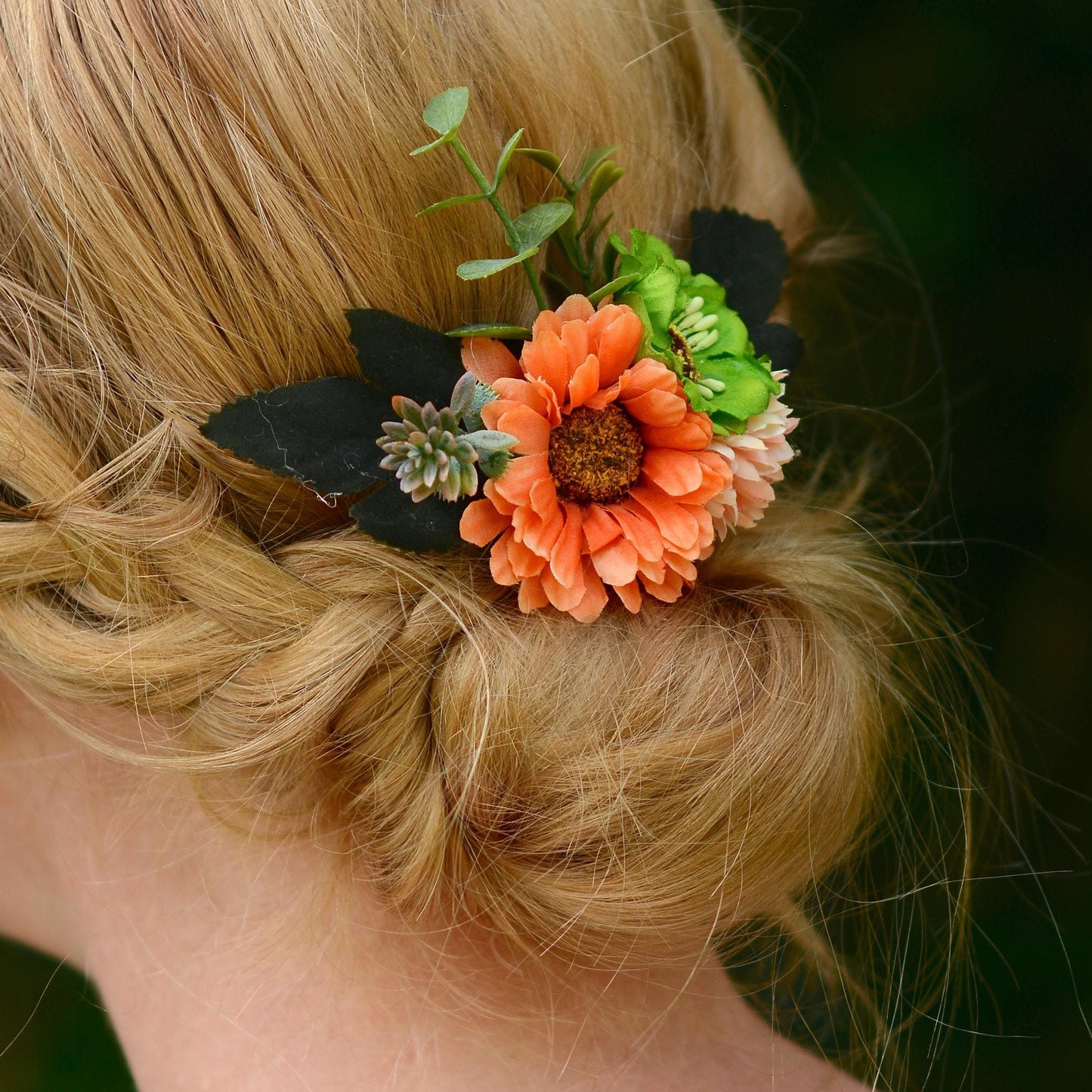 Floral hair accessory with orange flower and green leaves in a braided hairstyle.