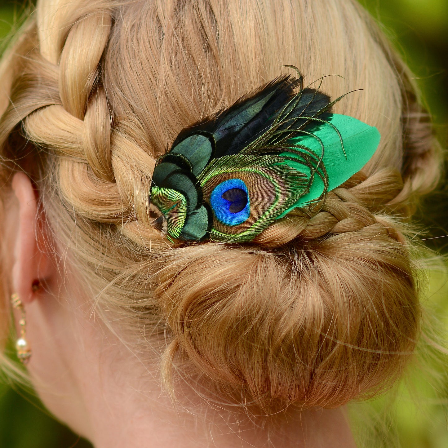 blonde braided wedding hair with feather hair piece with peacock eye in emerald green gold and blue 