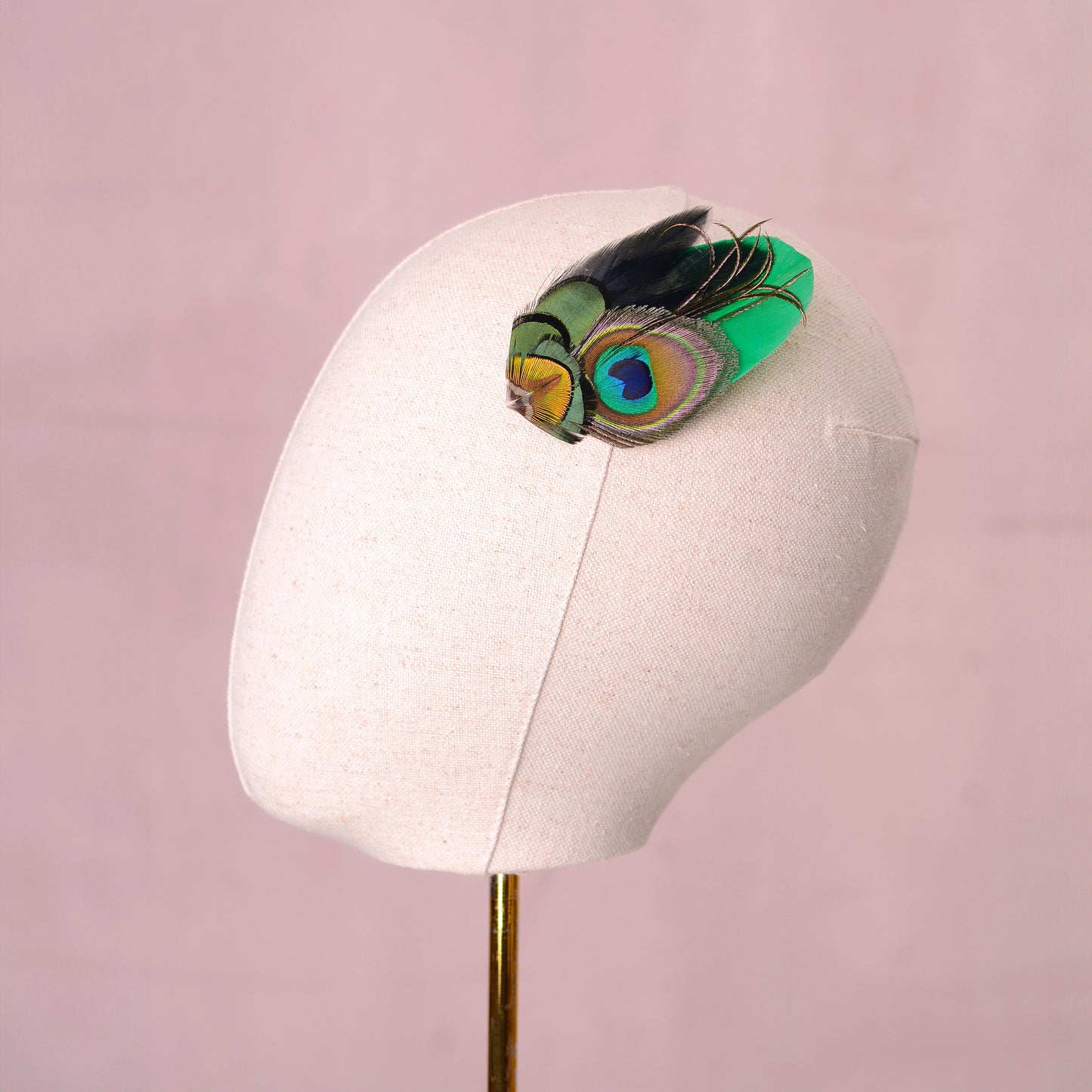 feather fascinator  with peacock eye in emerald green gold and blue  on a canvas mannequin head