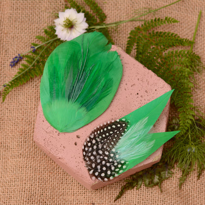 decorative feather hair clips in bright emerald green on a pink stone surrounded by plants on a burlap background