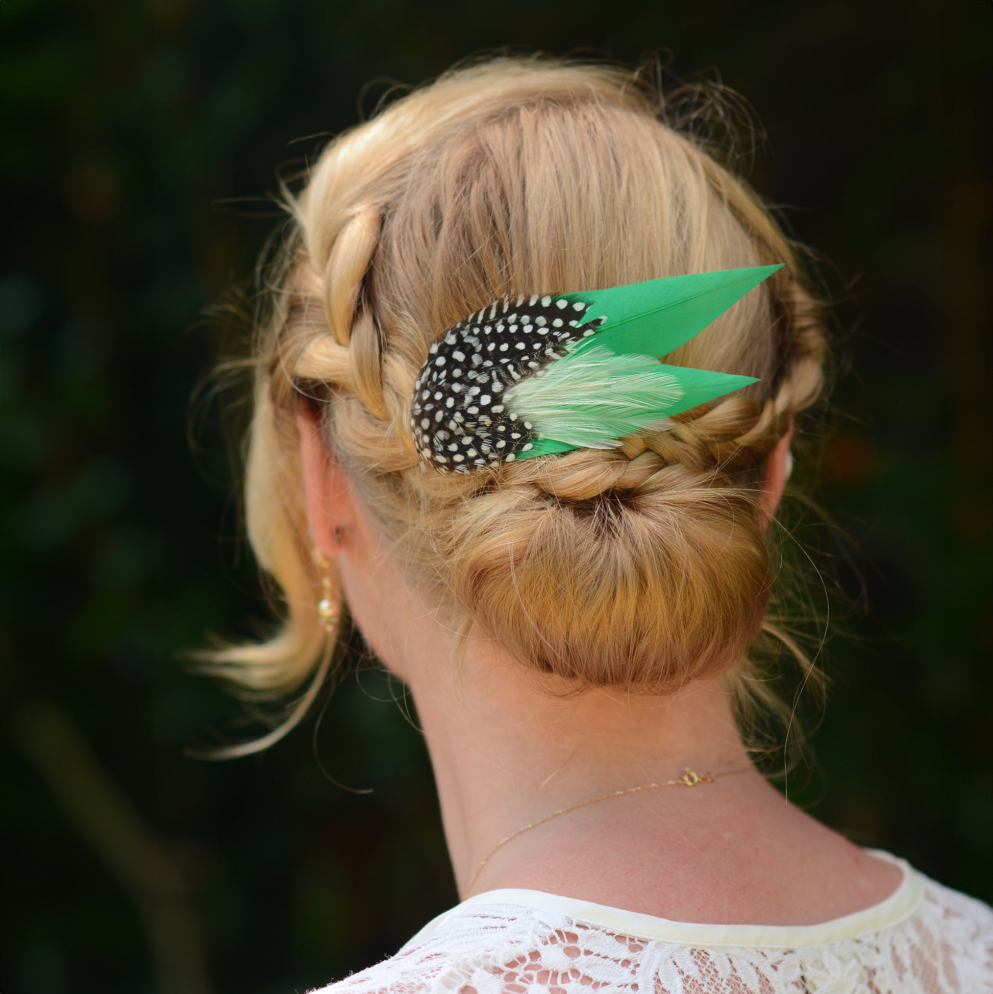 Woman with braided hairstyle with decorative green feather hair clip  with polka-dot spotted feathers