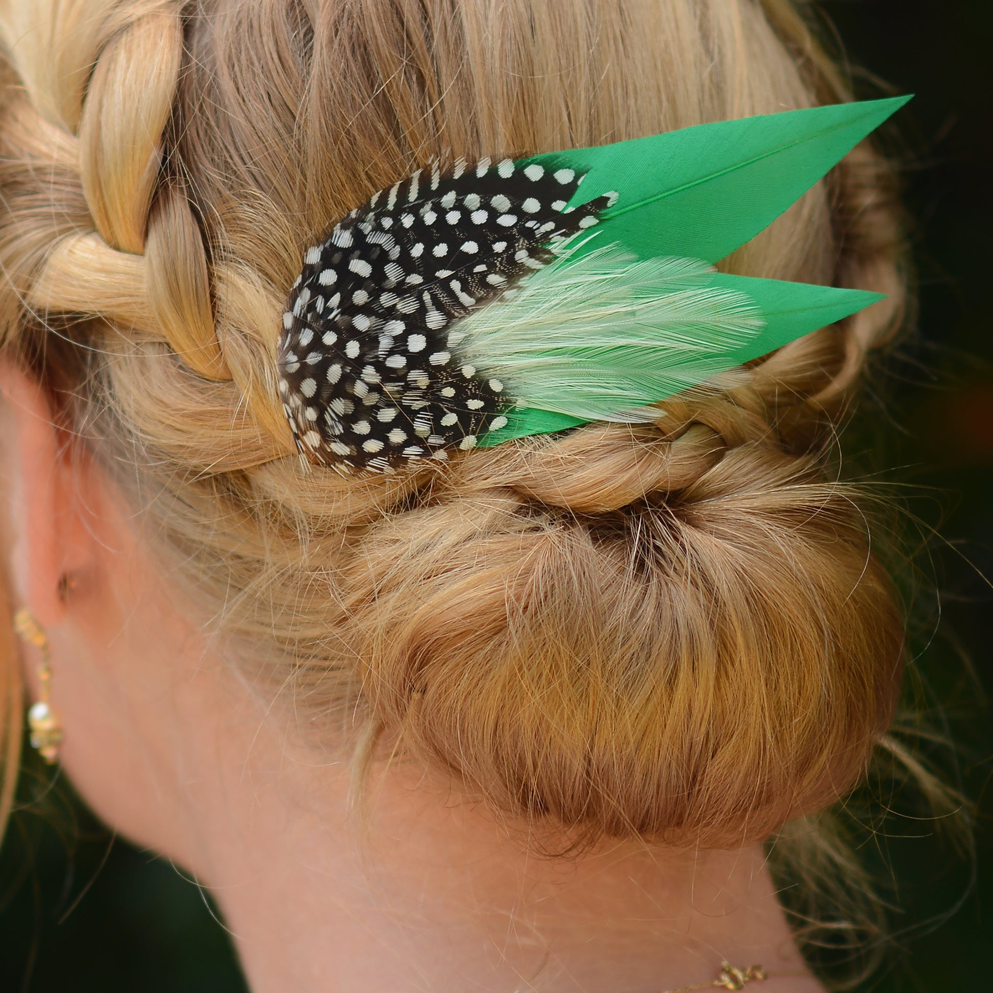 Close-up of a braided hairstyle with decorative green feather hair clip  with polka-dot spotted feathers