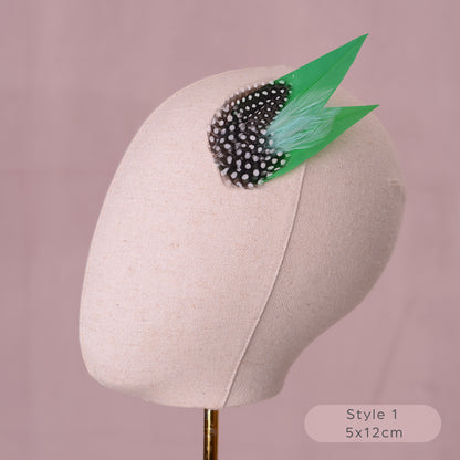 Green feathered hair clip with spotted polka dot feathers on a canvas mannequin head and blush pink background