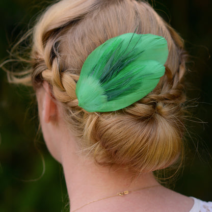 Person with braided hair wearing a green feather hair accessory against a dark background