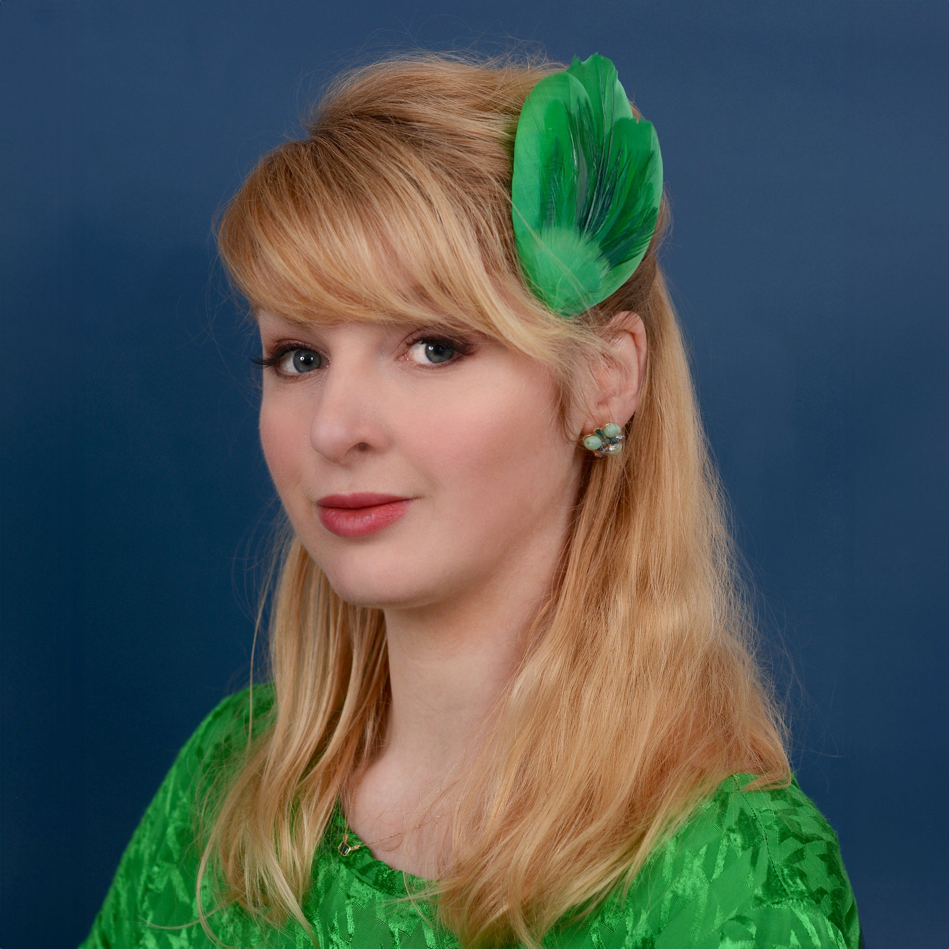 Woman with green feather hair accessory against a blue background