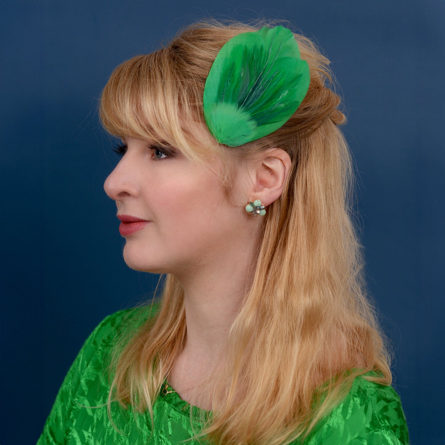 Woman with a green feathered hair accessory against a blue background