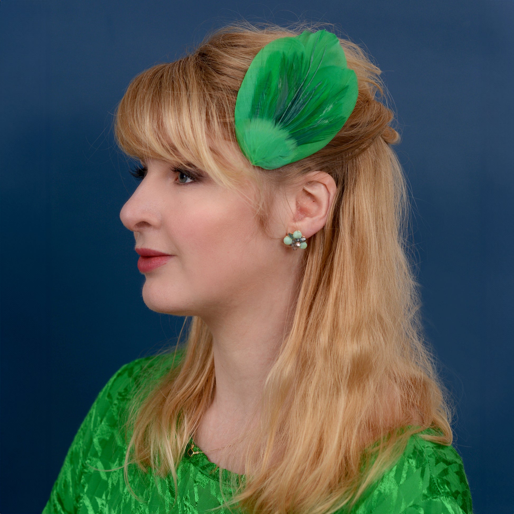 Woman with a green feathered hair accessory against a blue background