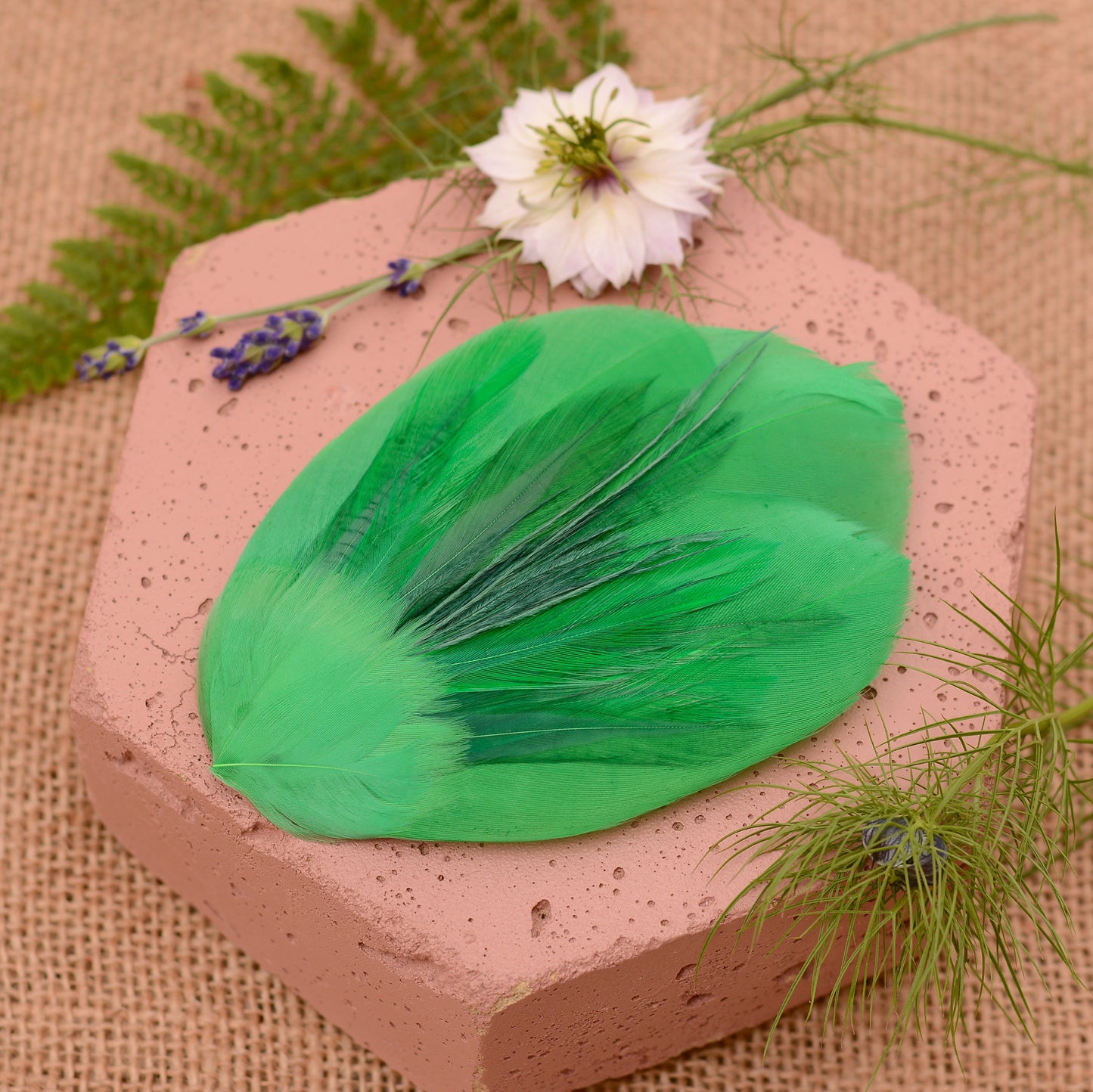 Green feathered hair clip on a textured surface with flowers and greenery.