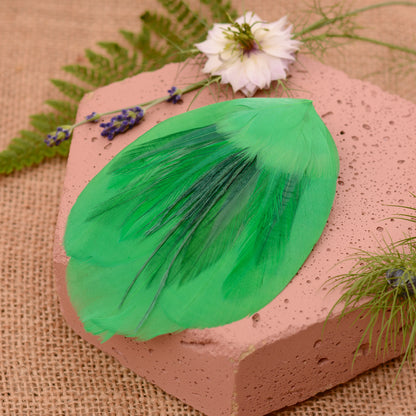 Green feathered hair clip on a textured surface with flowers and greenery.