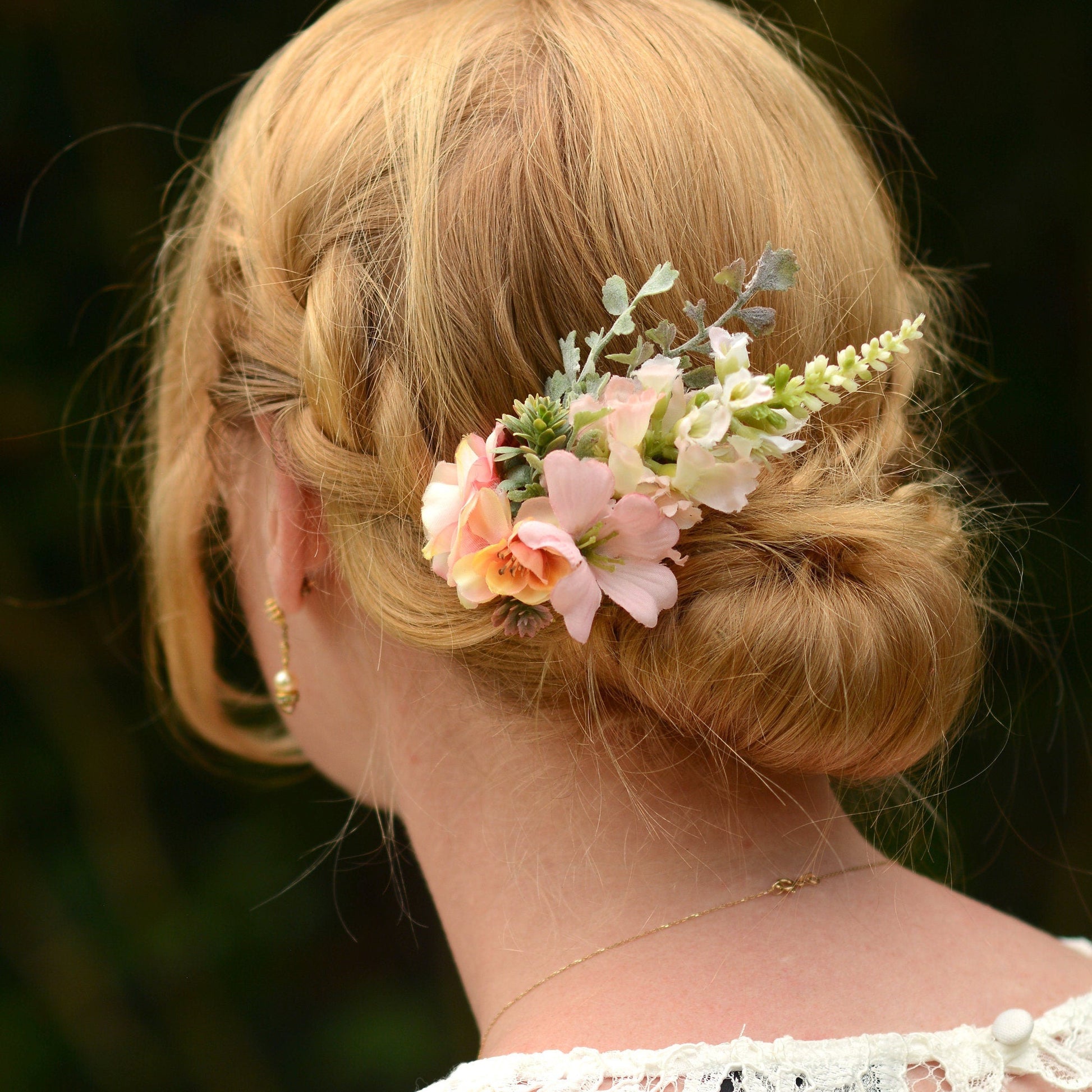 A hair clip with blush pink flowers and silver greenery, secured in a bride's updo hairstyle.
