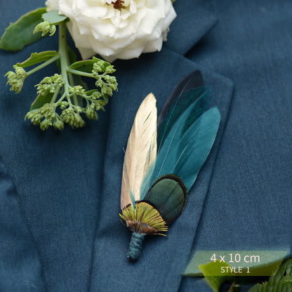 Teal, green and gold feather lapel pin brooch on a teal stuit jacket surounde by greenery.