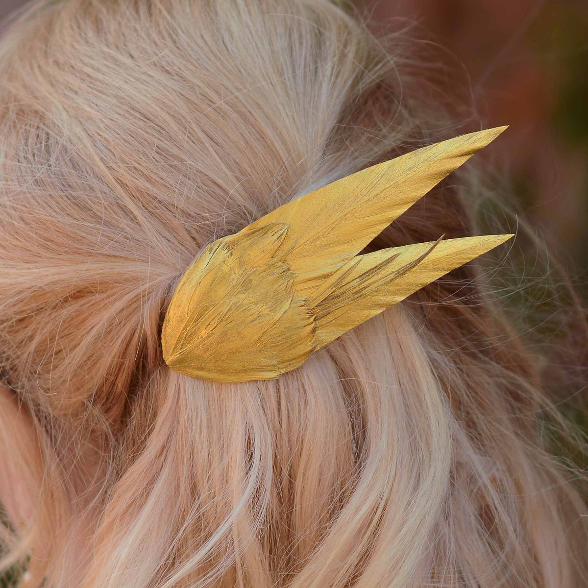 A elegant hair accessory of hand painted gold feathers attached, clipped into light blonde hair.
