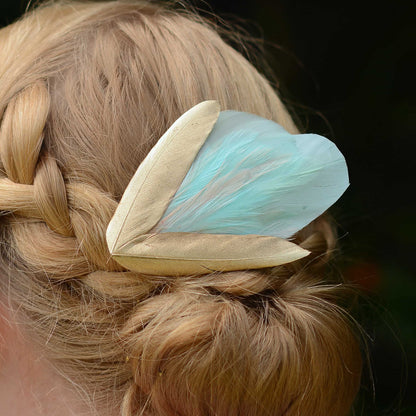 close up of  braided hair  and a decorative mint green and gold feather hairpiece against a dark background