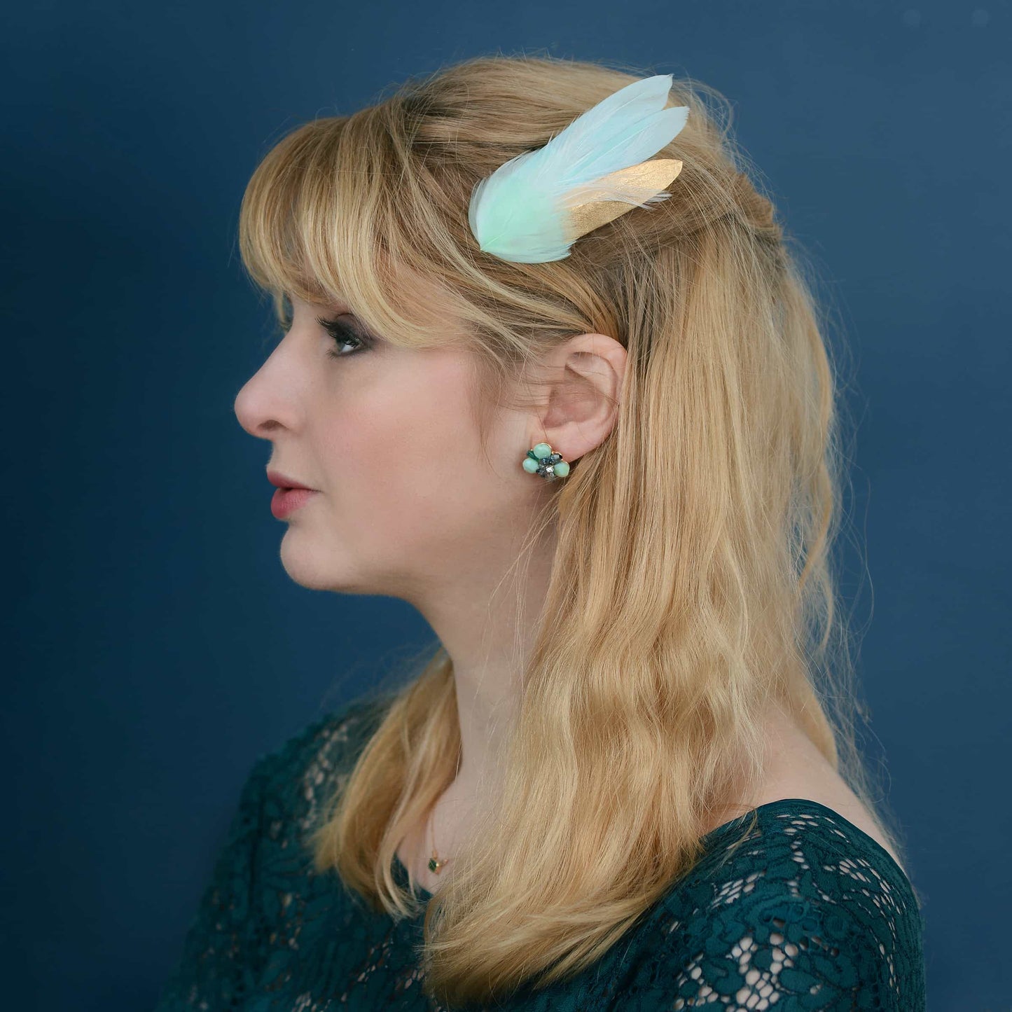 Woman with a decorative mint green and gold feather hair clip against a blue background