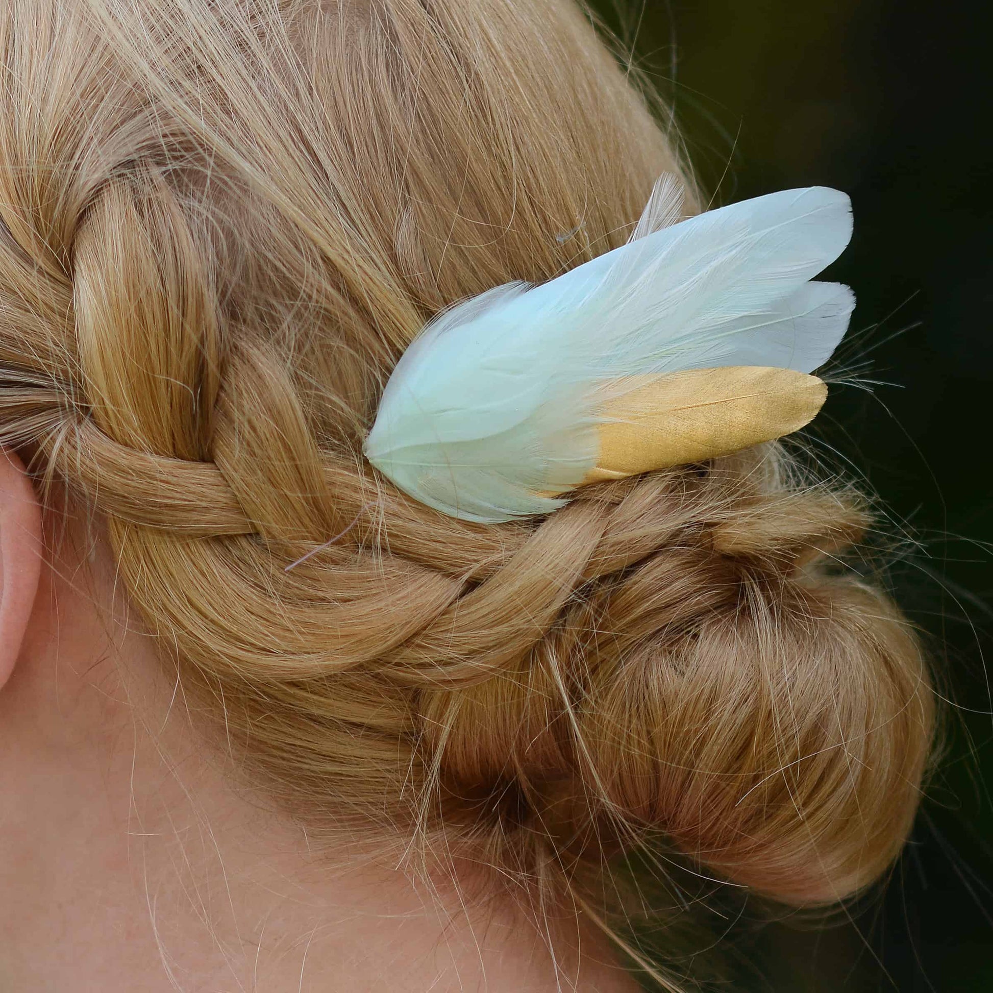 close up  of braided hair  and a decorative mint green and gold feather hairpiece against a dark background