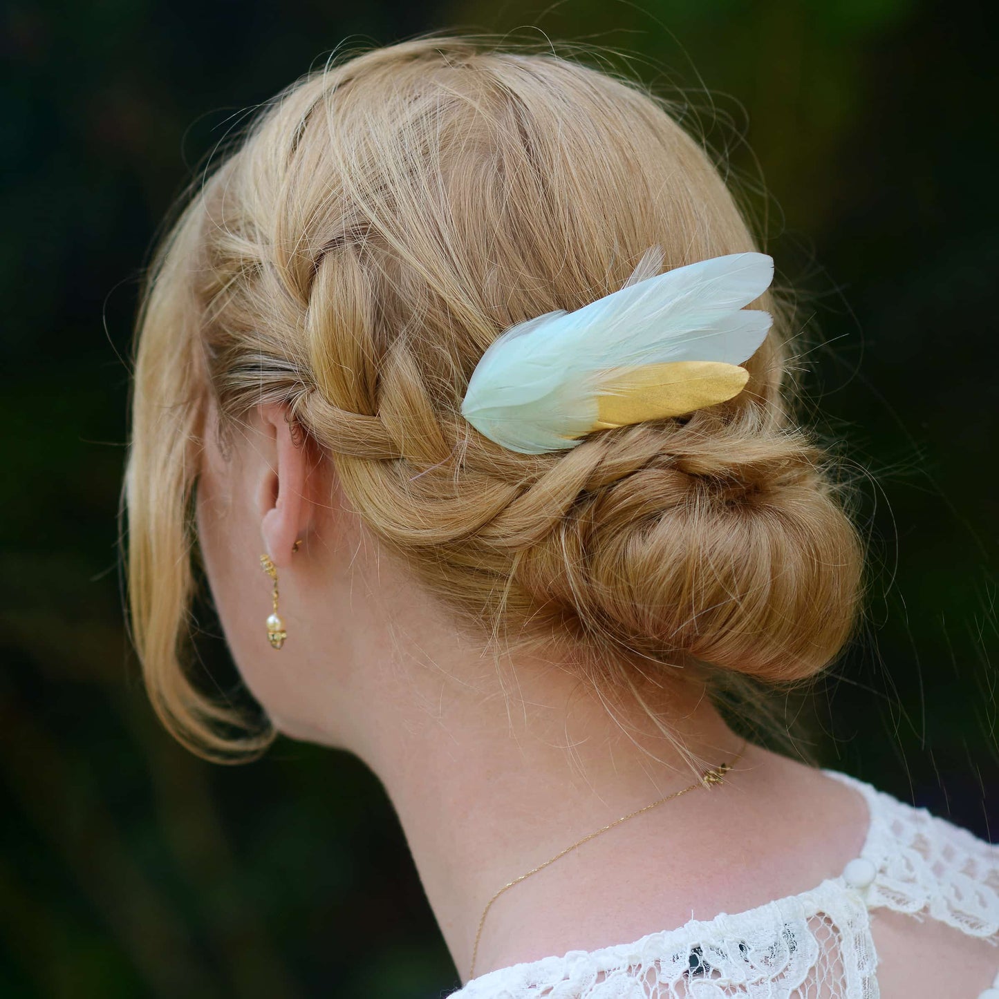 Person with braided hair  and a decorative mint green and gold feather hairpiece against a dark background