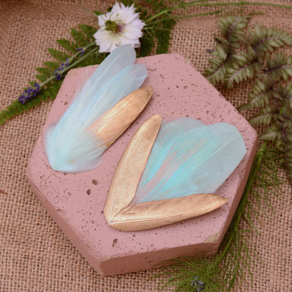 mint green and gold feather hair clips on a pink textured stone surrounded with burlap and flowers