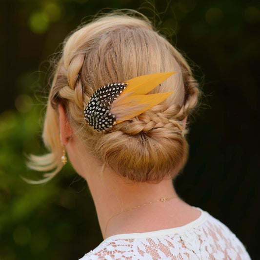 Woman with braided hair wearing a decorative feather hair clip ain gold yellow and polka dot feathers against a blurred natural background