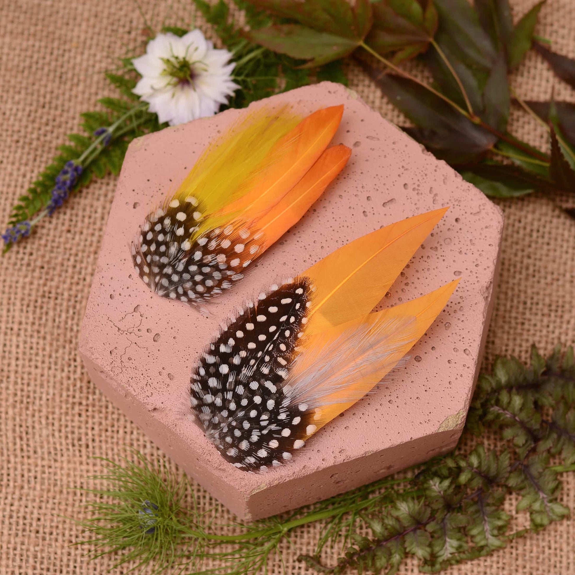 Feathered hair clip with mustard yellow and polka dot  feathers on a pink textured surface with greenery.