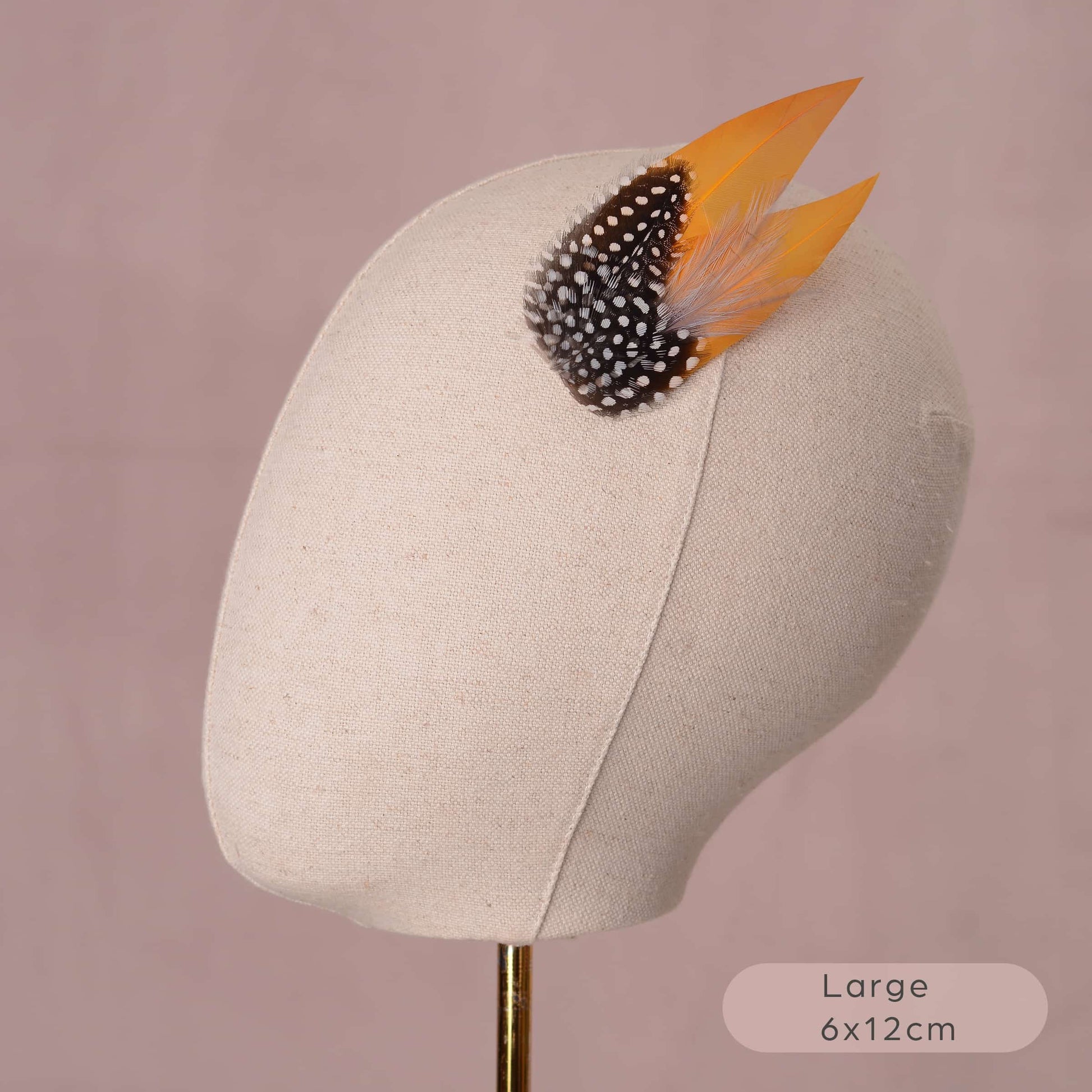 Small decorative headpiece in yellow gold and polka dot feathers on a mannequin head against a pink background