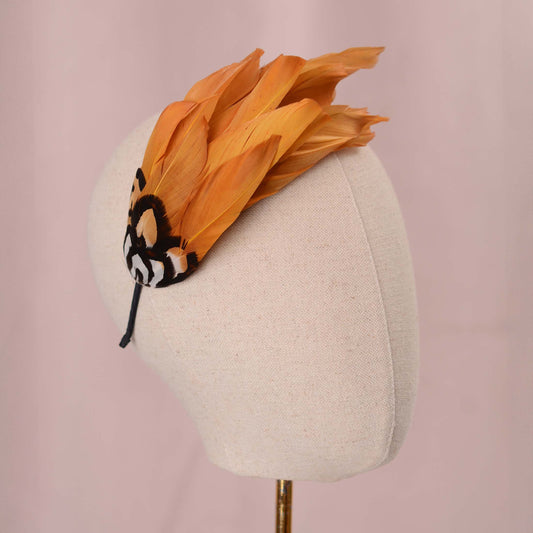 A gold-yellow feather fascinator headpiece in head against a soft pink background.