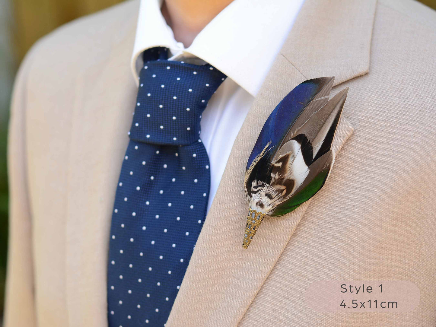 Close up of duck feather brooch pin with iridescent blue and green feathers on a beige jacket paired with a blue polka dot tie.