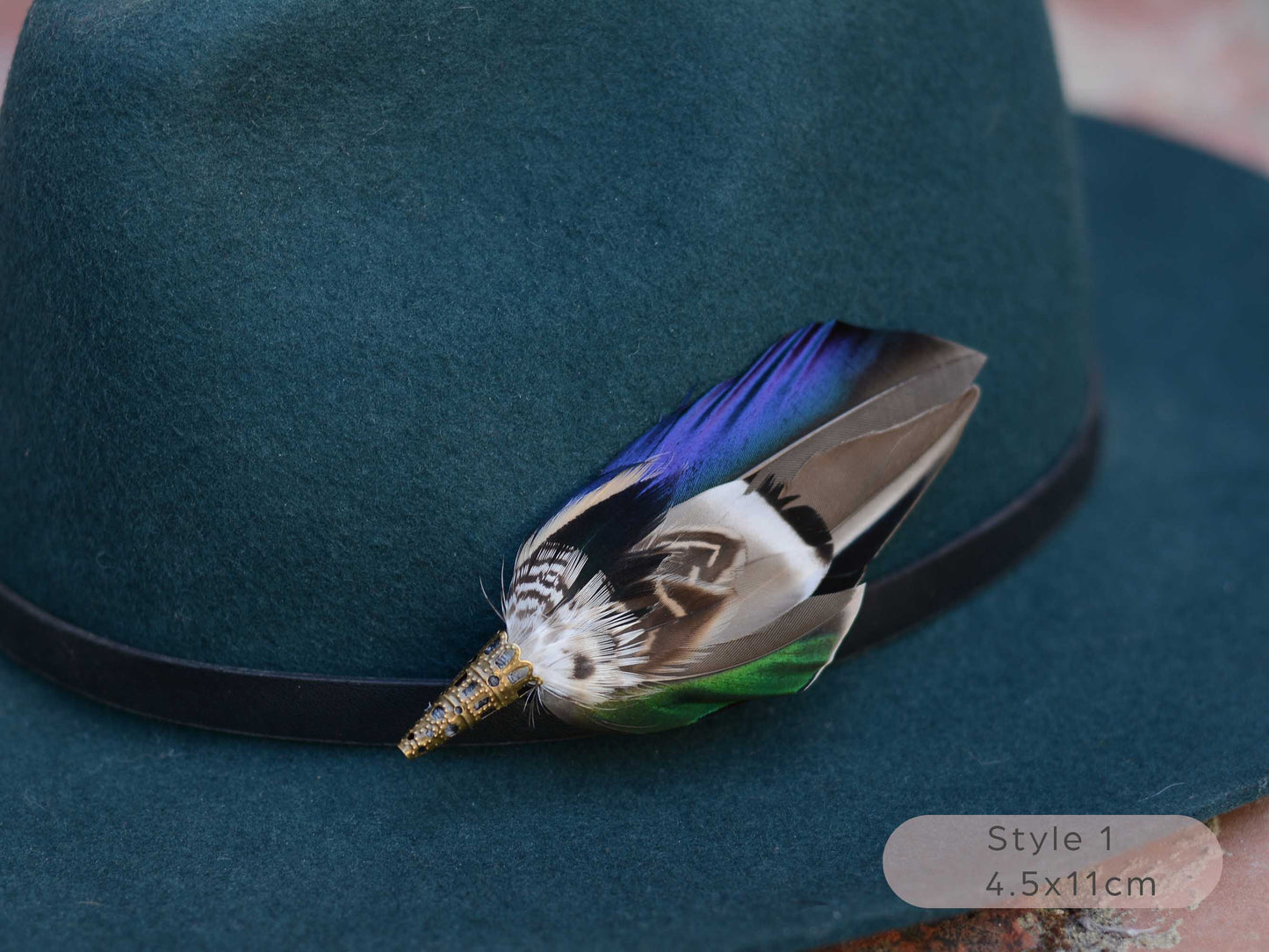 Close up of duck feather hat pin with iridescent blue and green feathers on a dark teal hat with a thin black leather hat band.