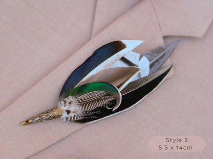 Large duck feather hat pin with iridescent blue and green feathers  with pointed brass cap on a beige jacket 