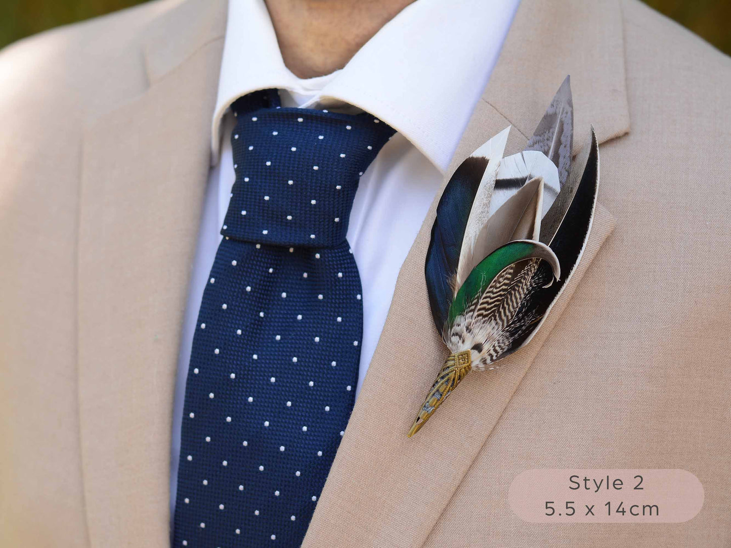 Large duck feather hat pin with iridescent blue and green feathers  with pointed brass cap on a beige jacket  with navy blue polka dot tie.