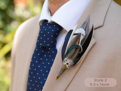 Large duck feather hat pin with iridescent blue and green feathers  with pointed brass cap on a beige jacket  with navy blue polka dot tie.