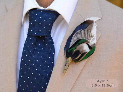 Large duck feather hat pin with iridescent blue and green feathers  with pointed brass cap on a beige jacket  with navy blue polka dot tie.
