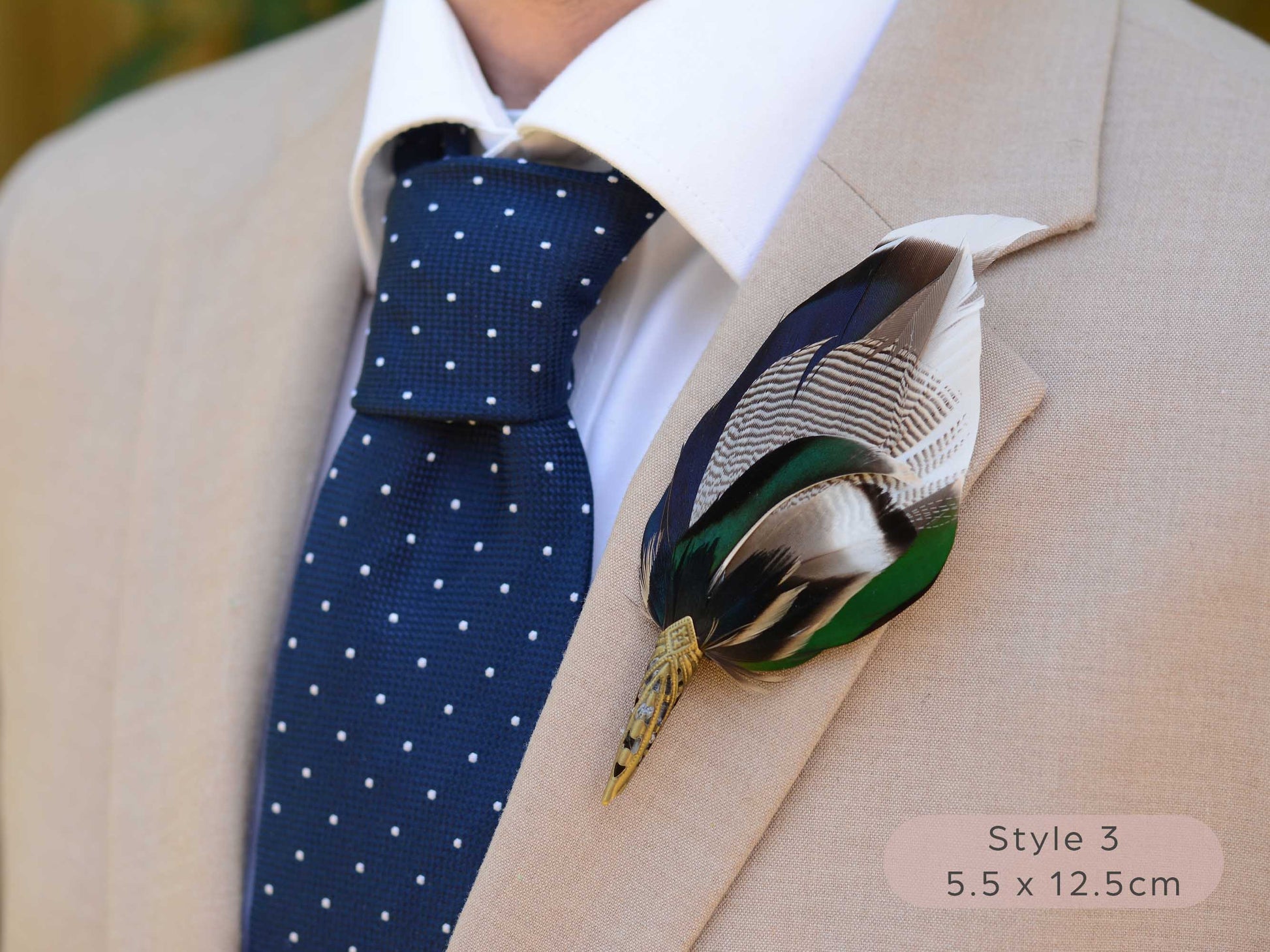 Large duck feather hat pin with iridescent blue and green feathers  with pointed brass cap on a beige jacket  with navy blue polka dot tie.