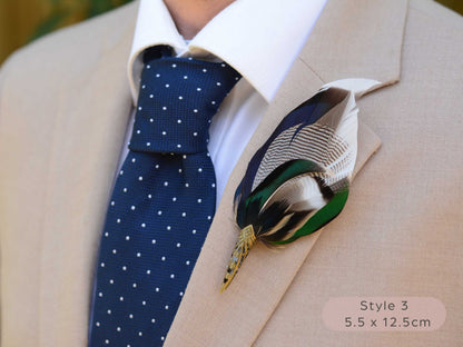Large duck feather hat pin with iridescent blue and green feathers  with pointed brass cap on a beige jacket  with navy blue polka dot tie.