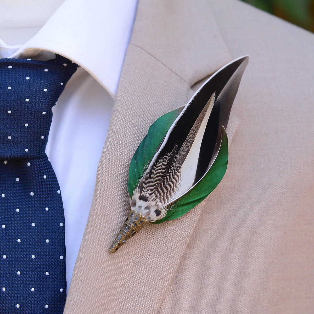 A duck featherlapel pin styled on a beige suit jacket, worn with a white dress shirt and a navy blue polka dot tie.
