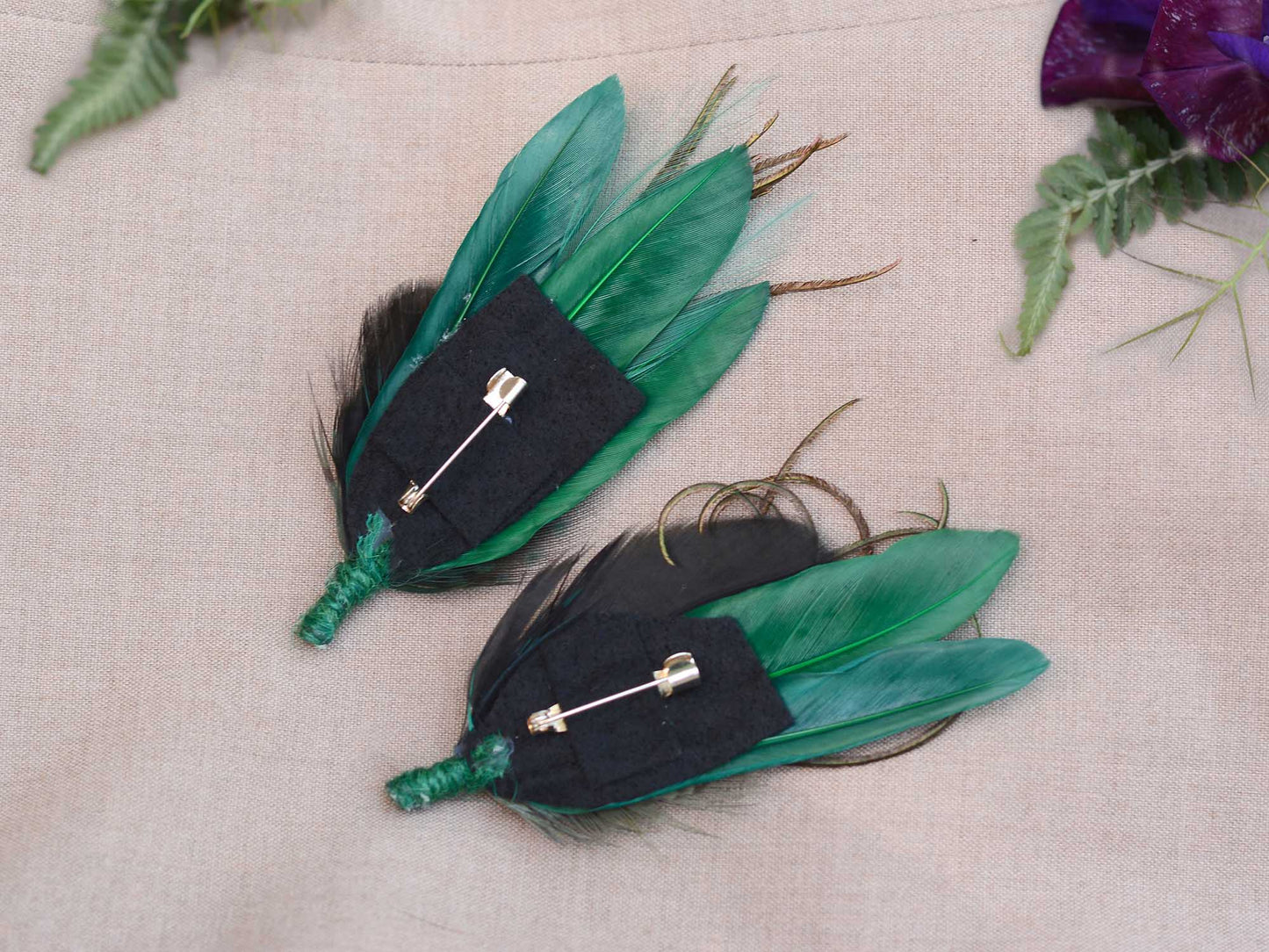 Two green feathered boutonnieres on a light background