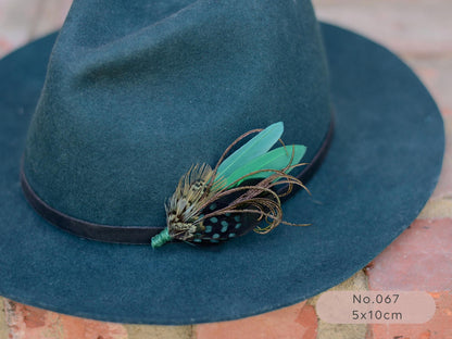 Teal fedora wool hat with a green pheasant, duck and peacock feather hat pin brooch on a  brick surface