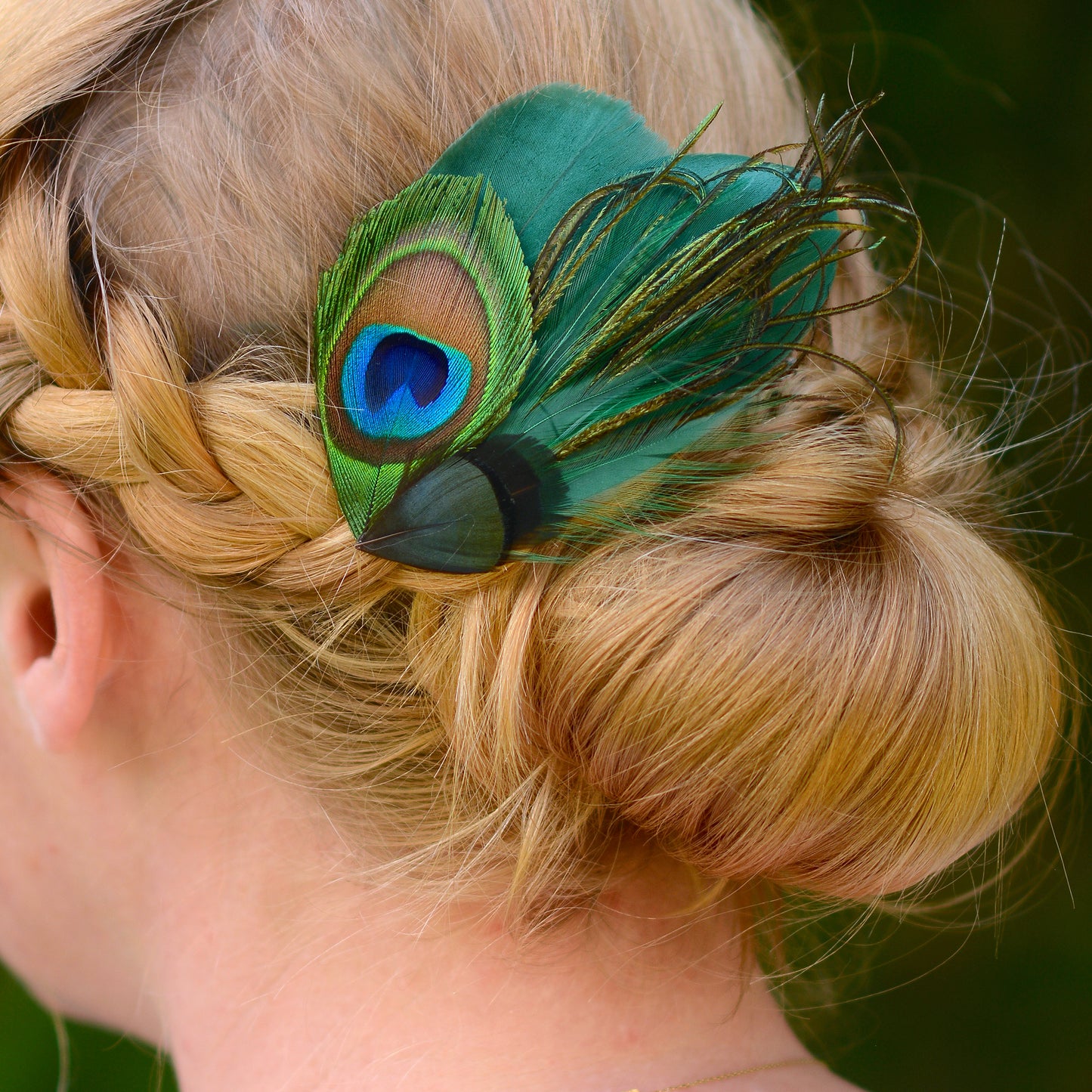 Person with braided hair wearing a green peacock and goose feather hair clip.