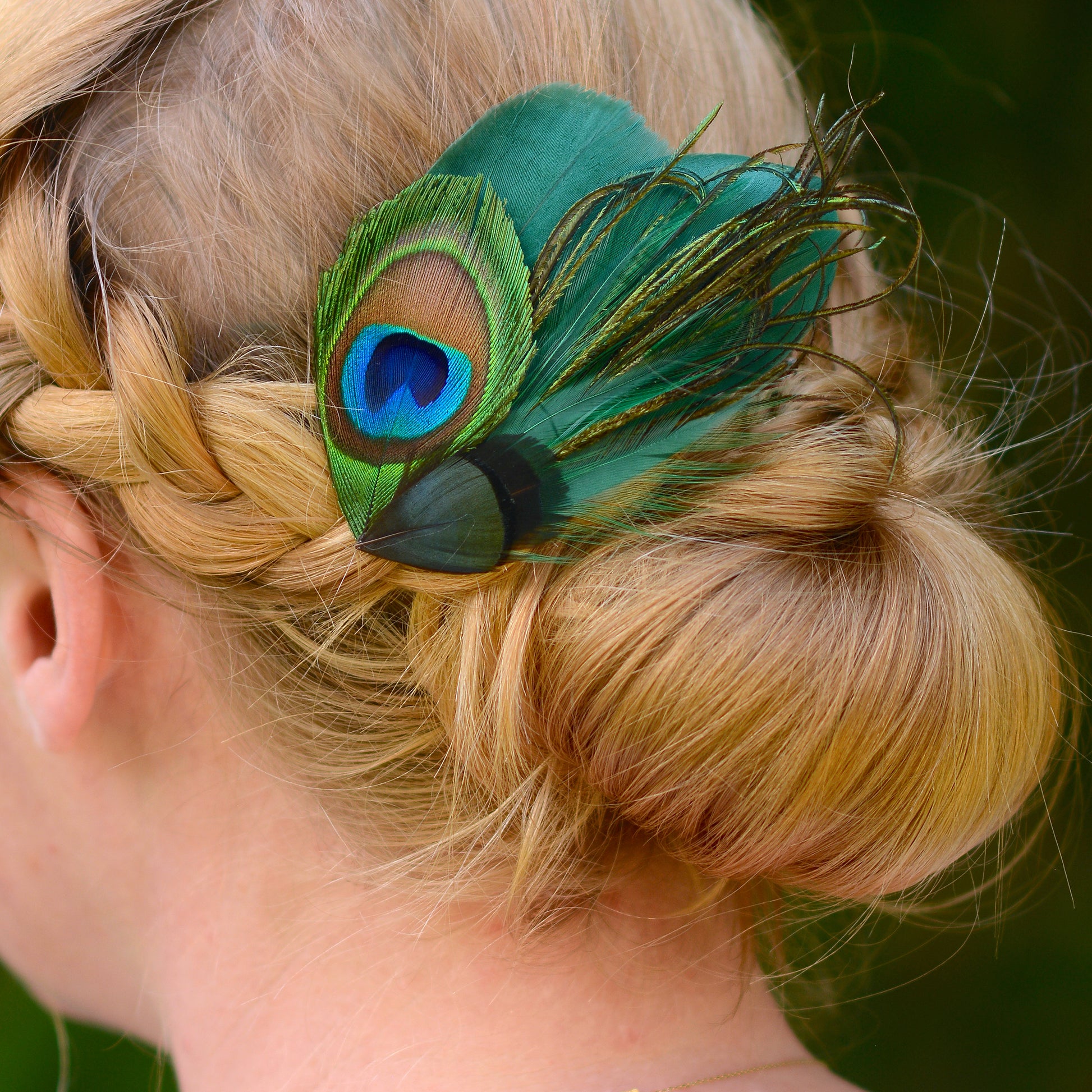 Person with braided hair wearing a green peacock and goose feather hair clip.