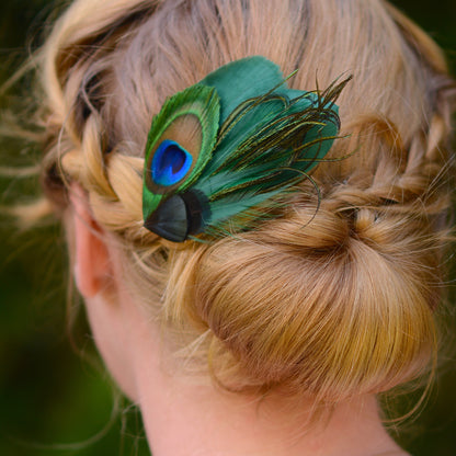 Person with braided hair wearing a green peacock feather hair clip.