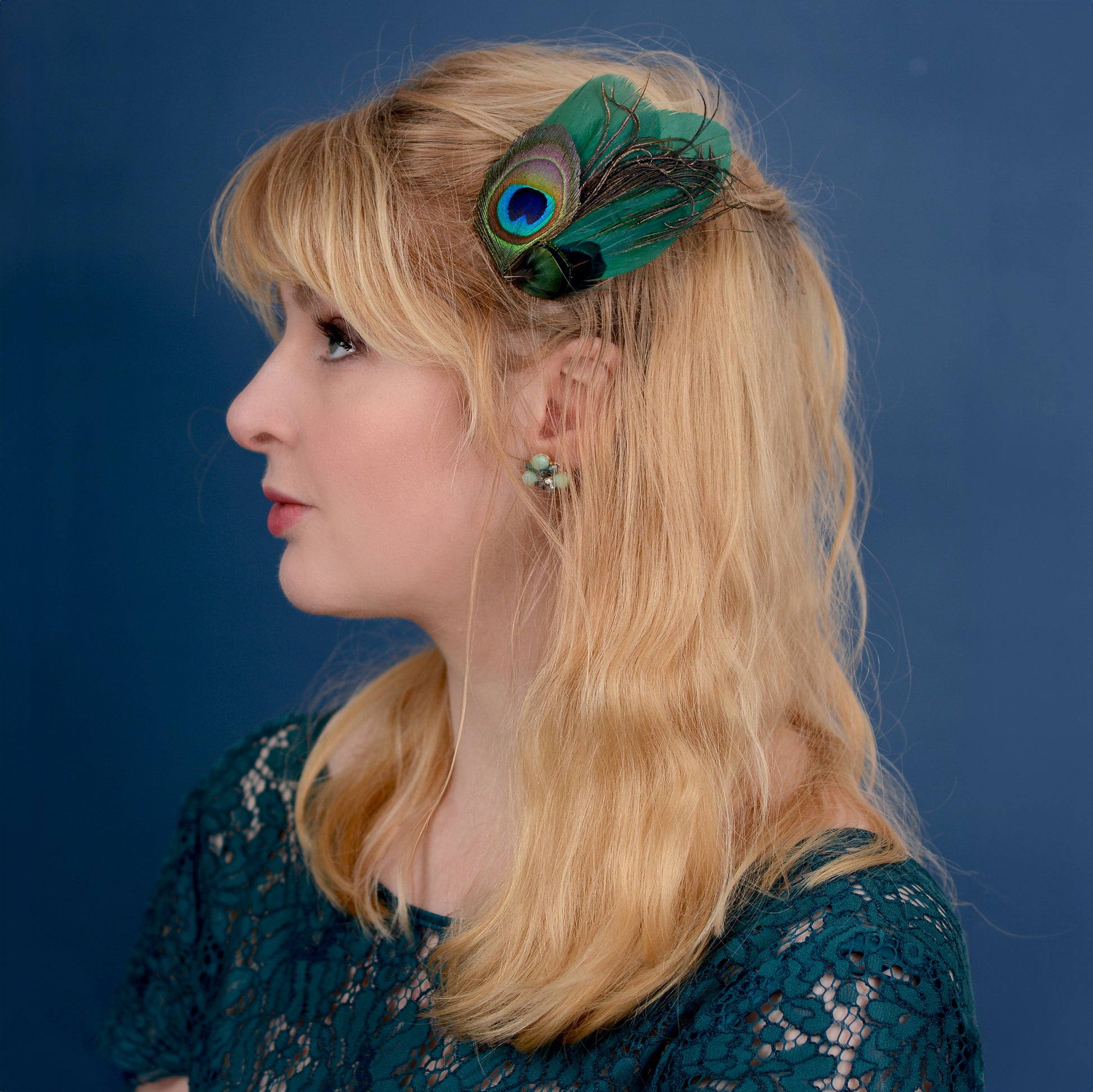 Woman with a green peacock feather fascinator  against a blue background