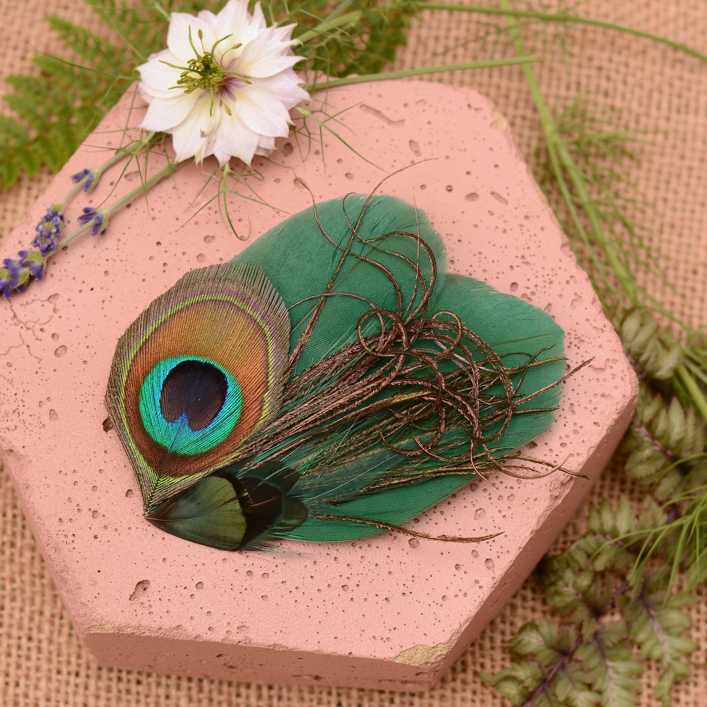 Green peacock feather hair clip on a pink stone with flowers and greenery