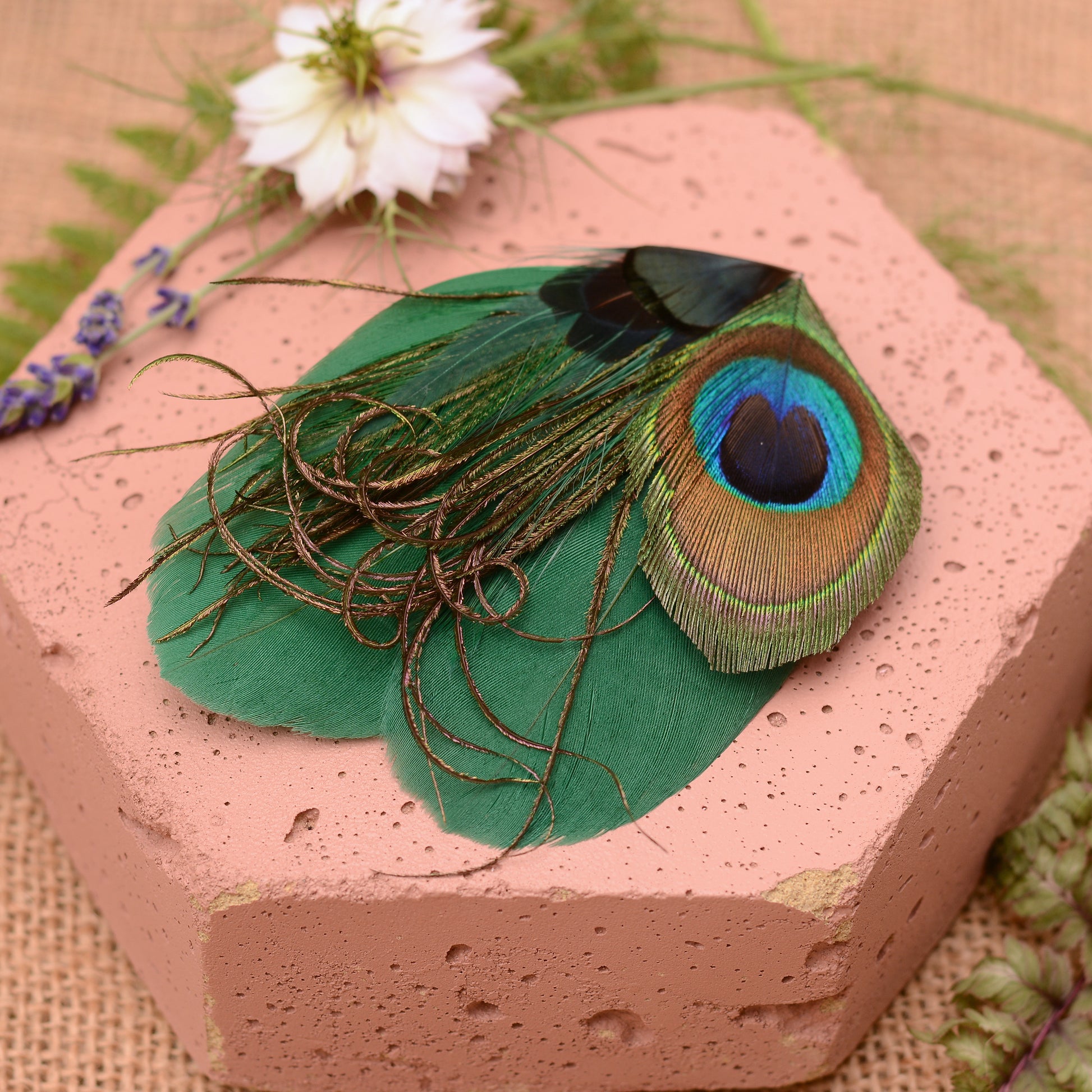 Green peacock feather hair clip on a pink stone with flowers and greenery
