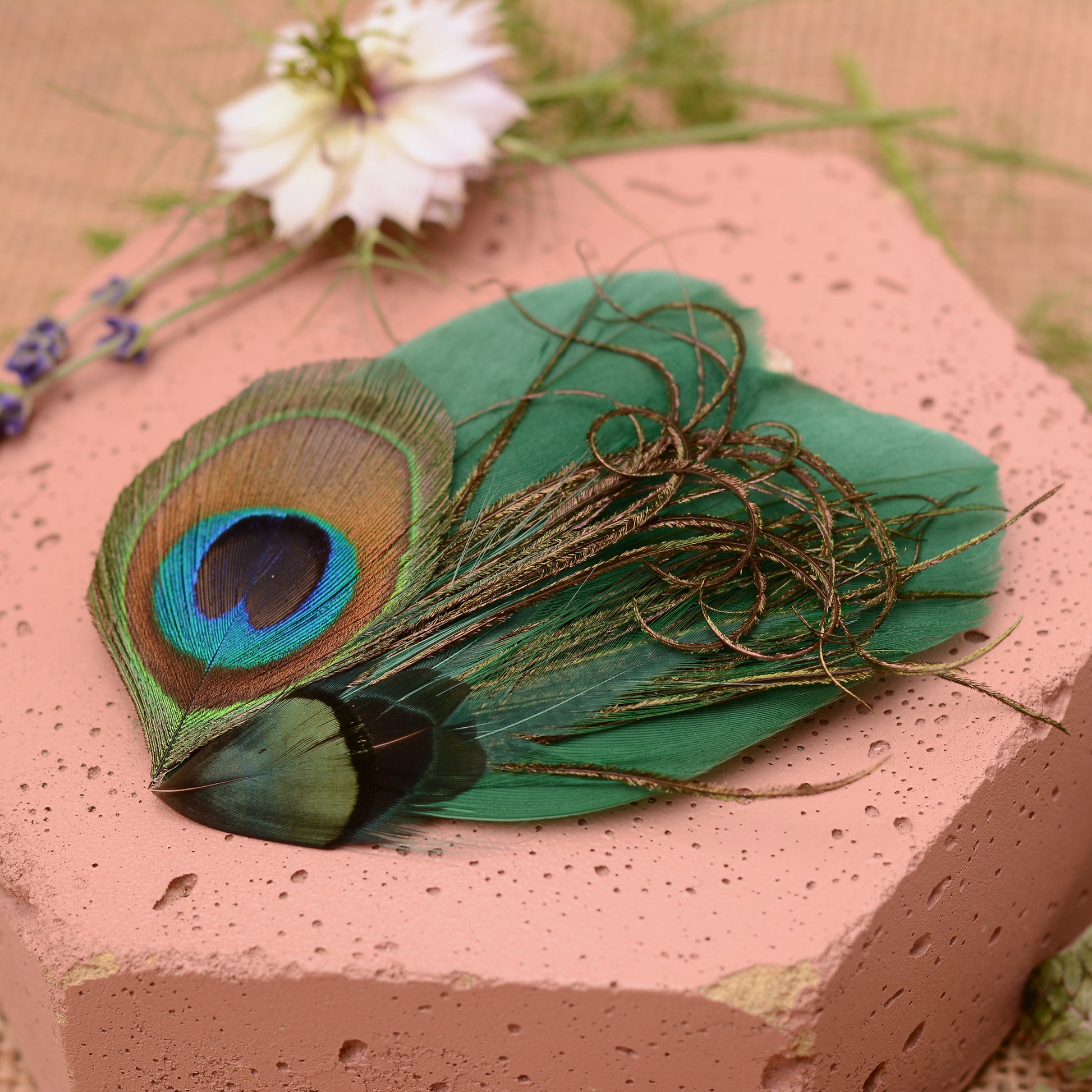 Green peacock feather hair clip on a pink stone with flowers and greenery